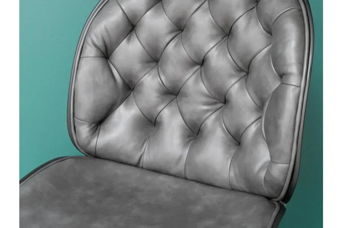 Grey tufted dining chair with padded backrest and seat against teal wall