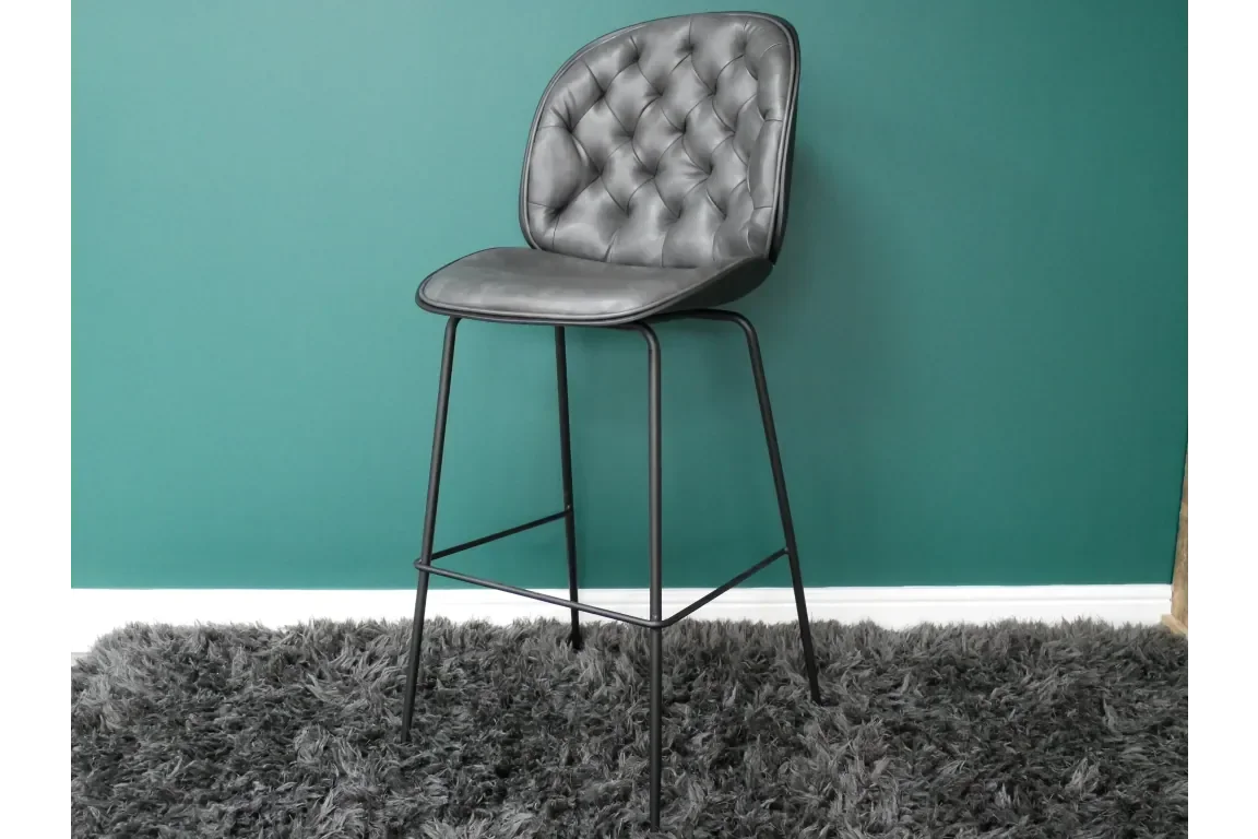 Grey leather bar stool with tufted back and black metal legs on shaggy rug