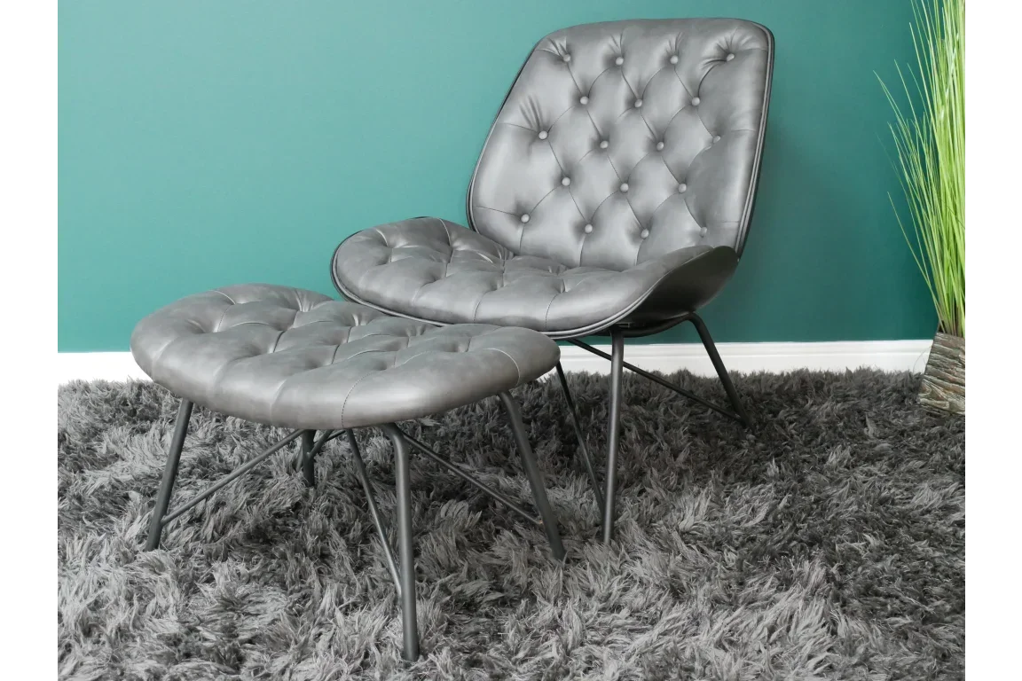 Tufted grey accent chair with matching footstool on shaggy rug against teal wall