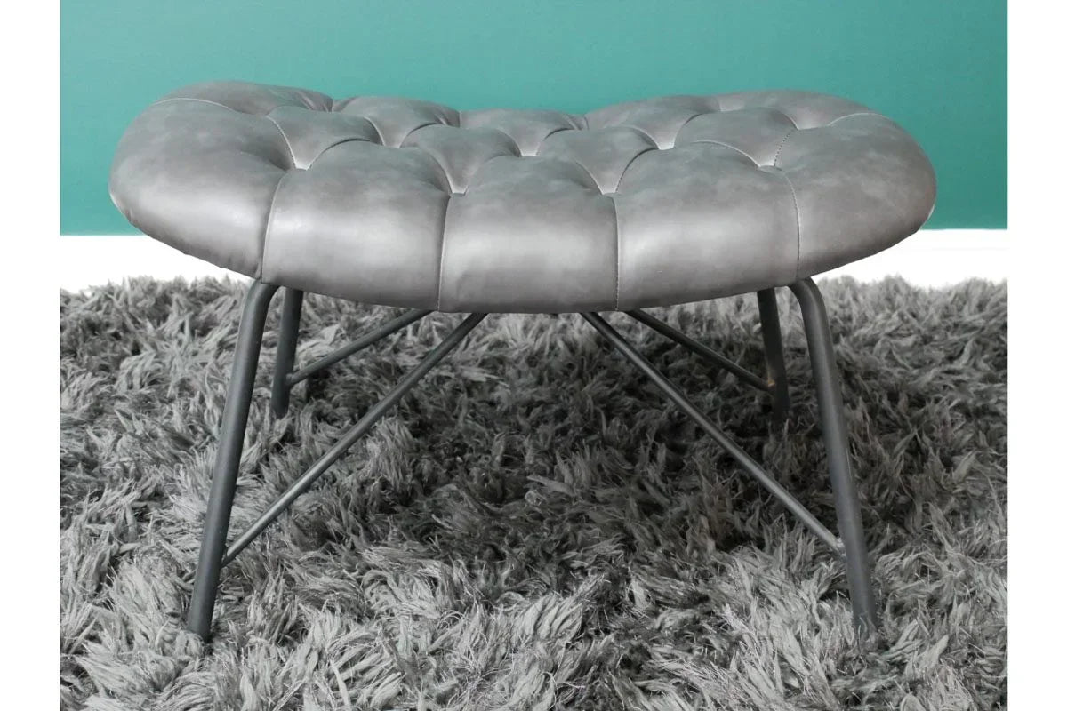 Round grey upholstered footstool with metal legs on a shaggy rug