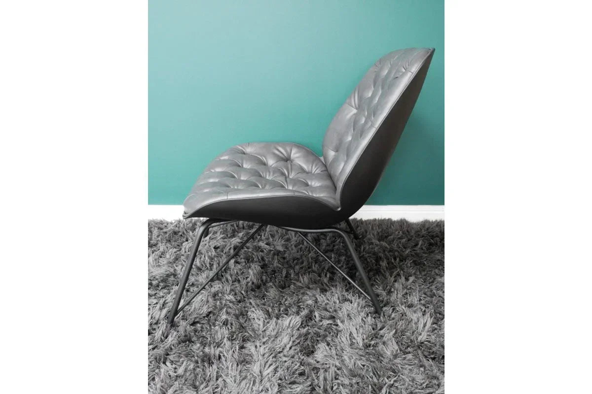 Tufted grey leather accent chair with black metal legs on a shaggy rug