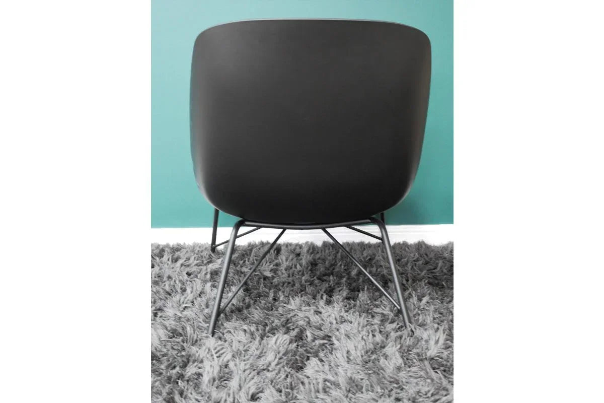Black modern dining chair with curved plastic back and metal legs on grey rug