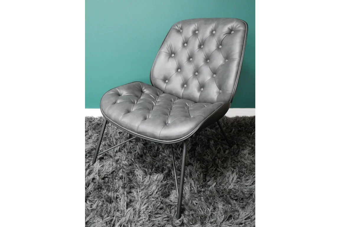 Grey accent chair with button-tufted upholstery and black metal legs on textured rug