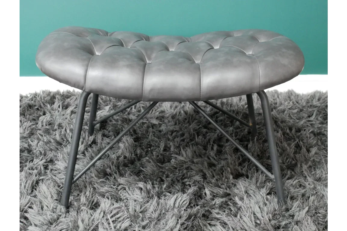 Grey leather ottoman with tufted seat and black metal legs on a shaggy rug
