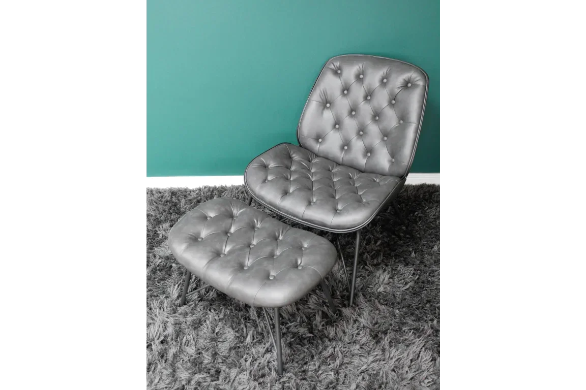 Grey leather accent chair with matching footstool on grey rug against teal wall