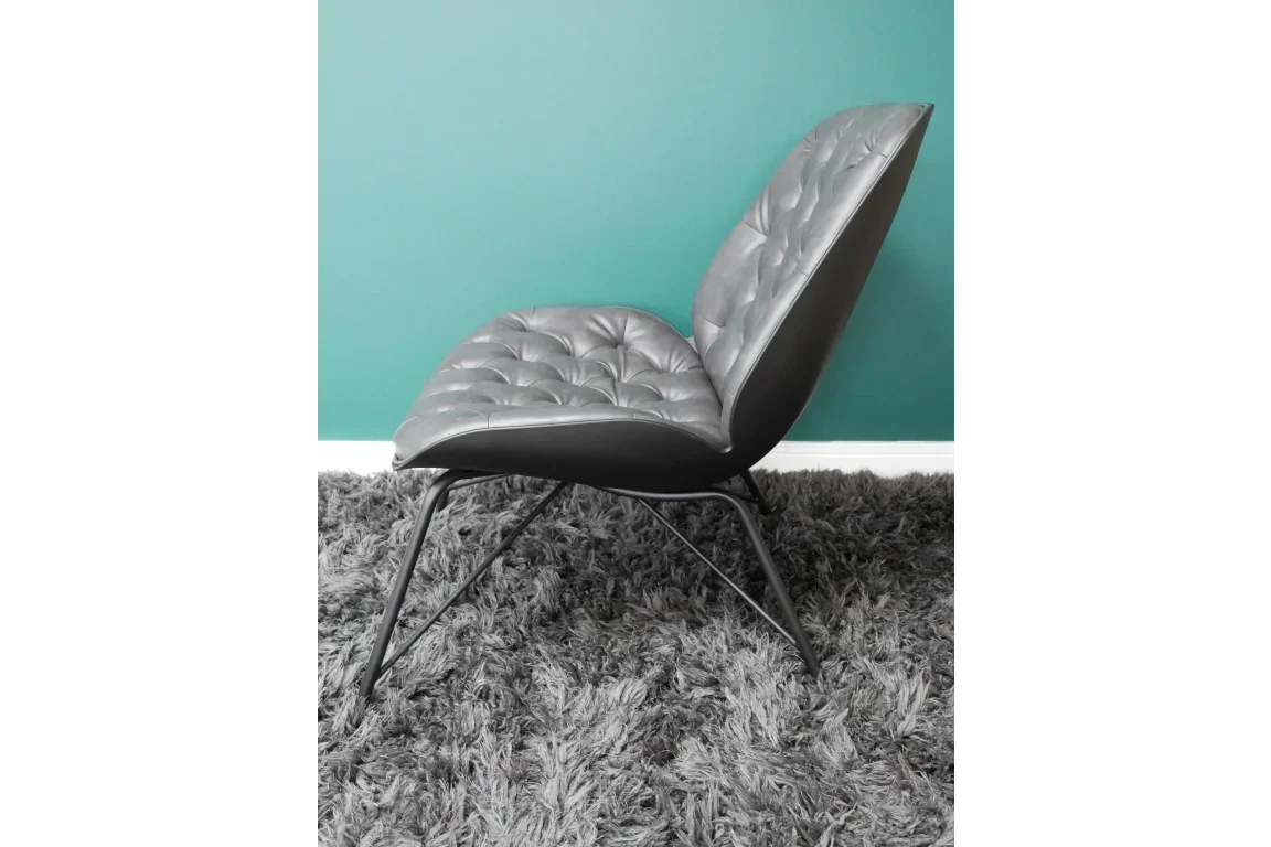 Grey leather accent chair with tufted upholstery and metal legs on a shaggy rug