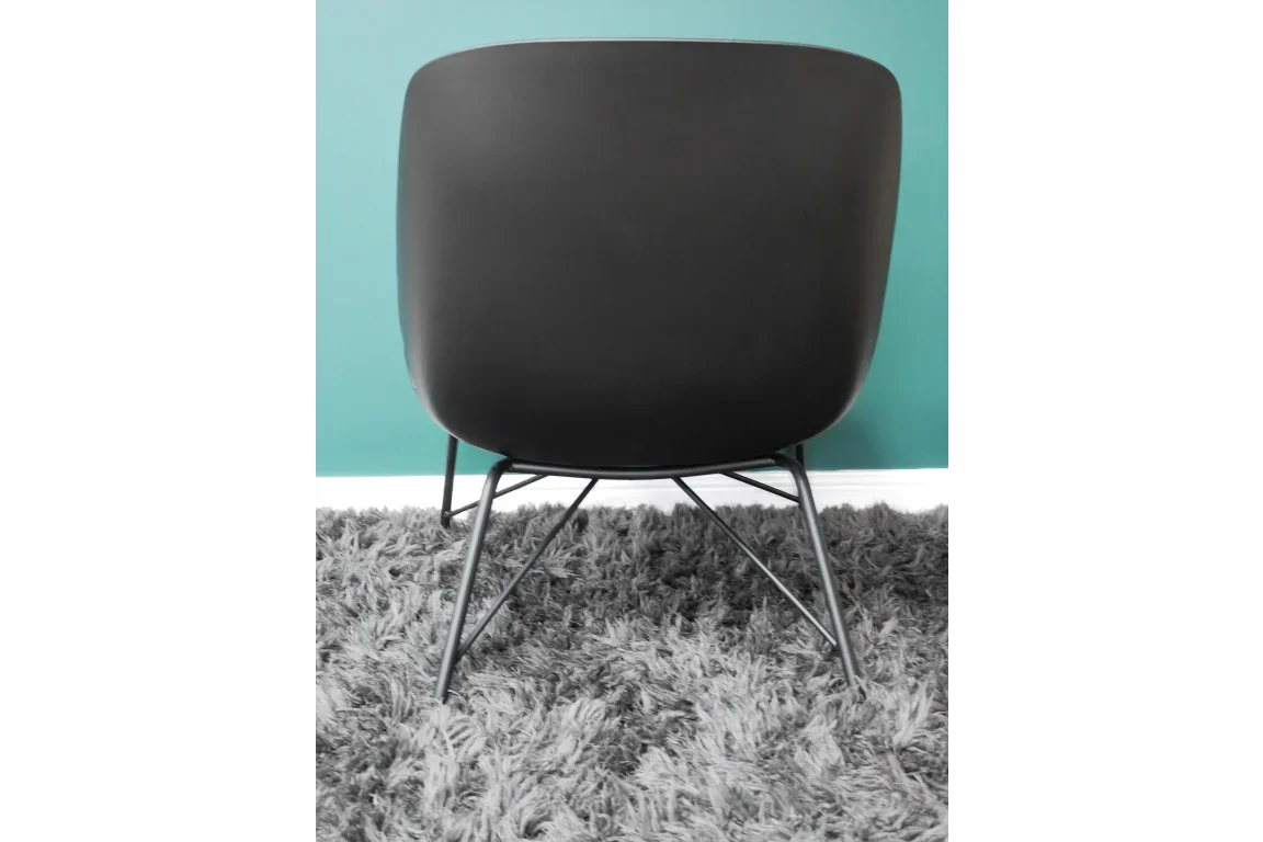 Black modern accent chair with metal legs on grey shaggy rug against teal wall