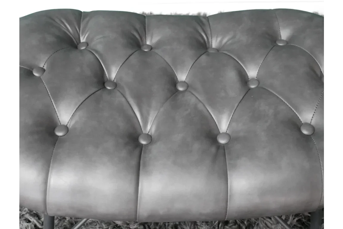 Close view of grey tufted ottoman with button detail and faux leather upholstery
