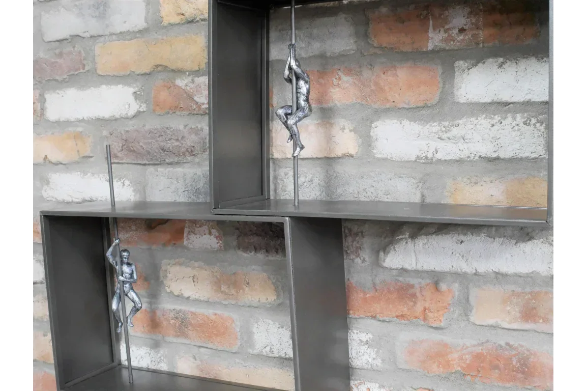 Industrial metal wall shelf with two silver climbing figures against exposed brick