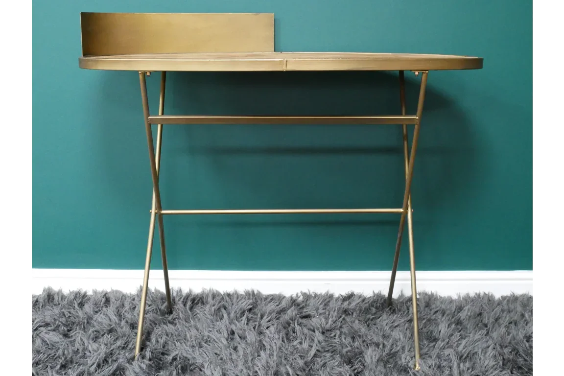 Gold metal console table with slim legs and raised back panel against teal wall