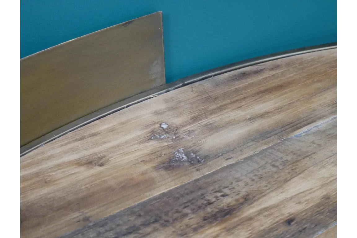 Close-up of wood dining table top with brown metal trim against teal wall