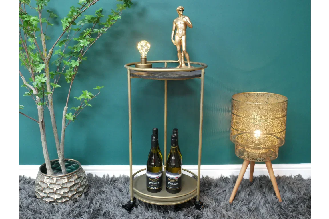 Round gold side table with two wine bottles, lamp, and statue against teal wall