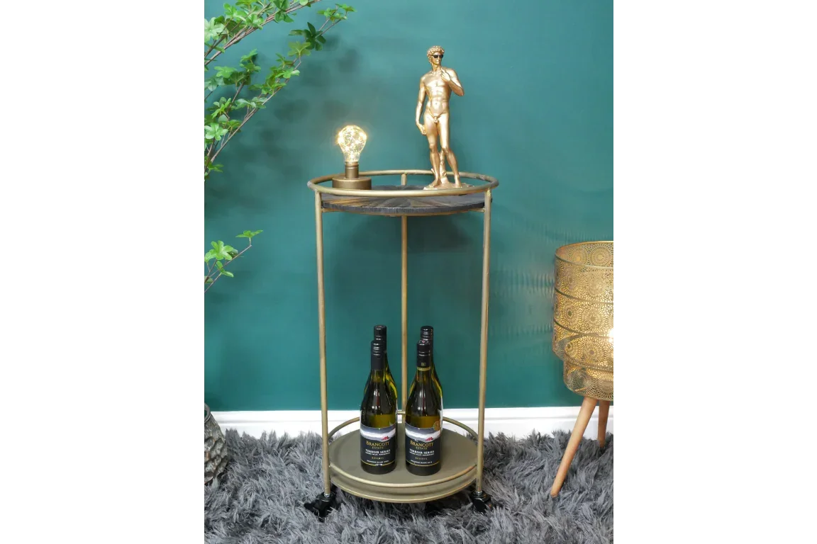 Gold metal bar trolley with black top shelf, ornament, lamp, and wine bottles on lower shelf