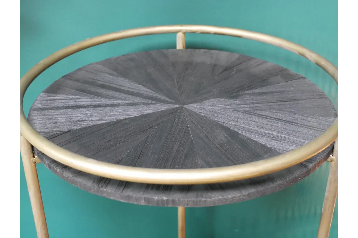 Round side table with black wood top and gold metal frame against teal wall