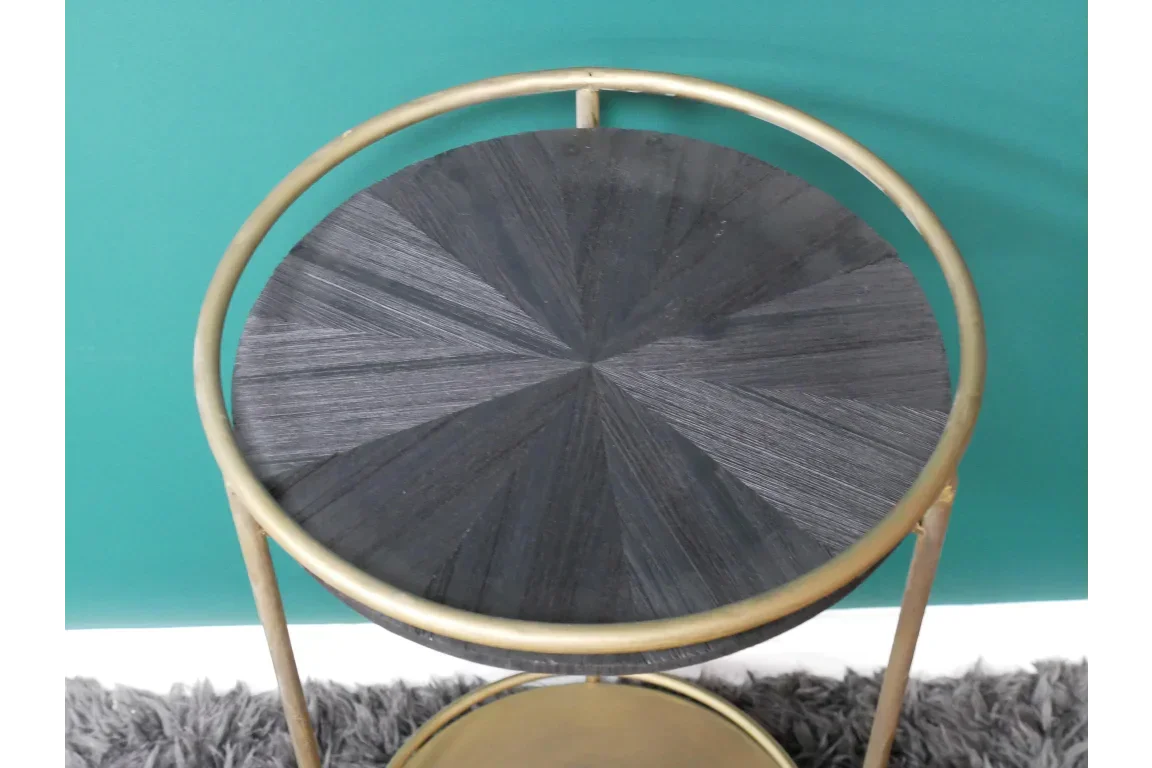 Round black wood side table with gold metal frame against a teal wall on grey rug