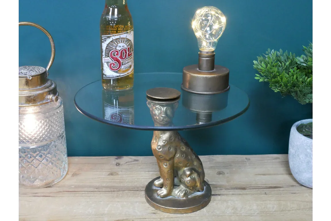 Round glass side table with gold leopard base on wooden surface