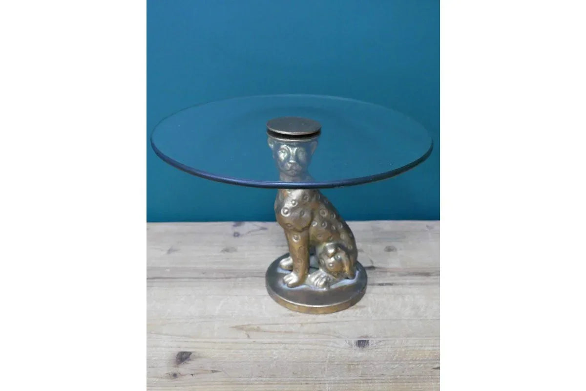 Round glass side table with gold cheetah base on wooden floor against teal wall