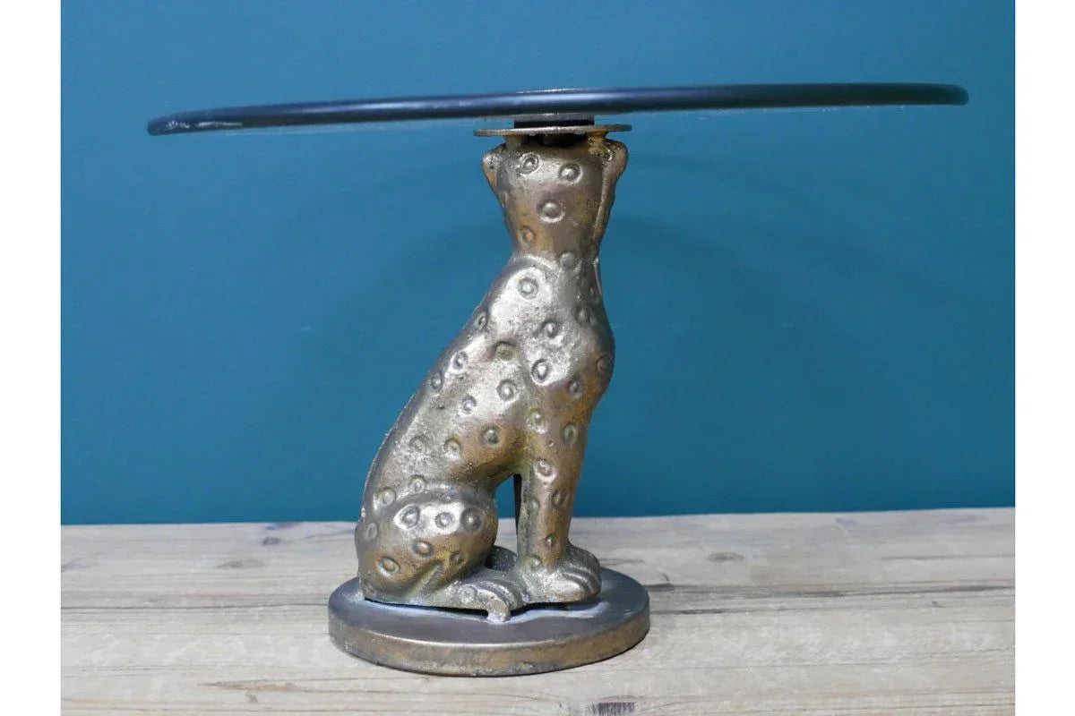 Gold metal cheetah side table with round glass top on wooden floor against blue wall