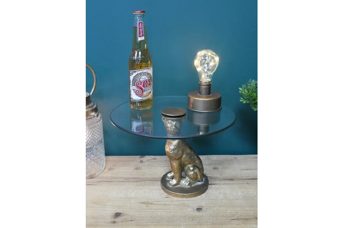 Glass side table with gold leopard base, styled with bottle and lamp on wooden surface
