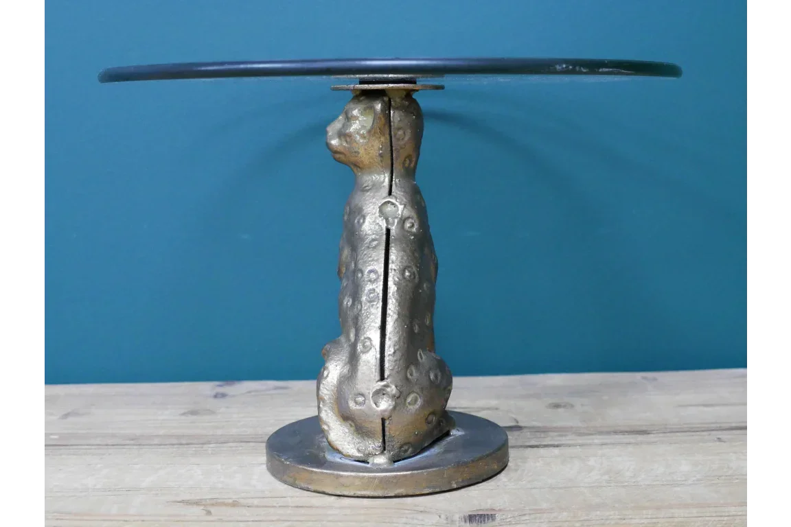 Round glass top side table with gold leopard statue base on wood surface