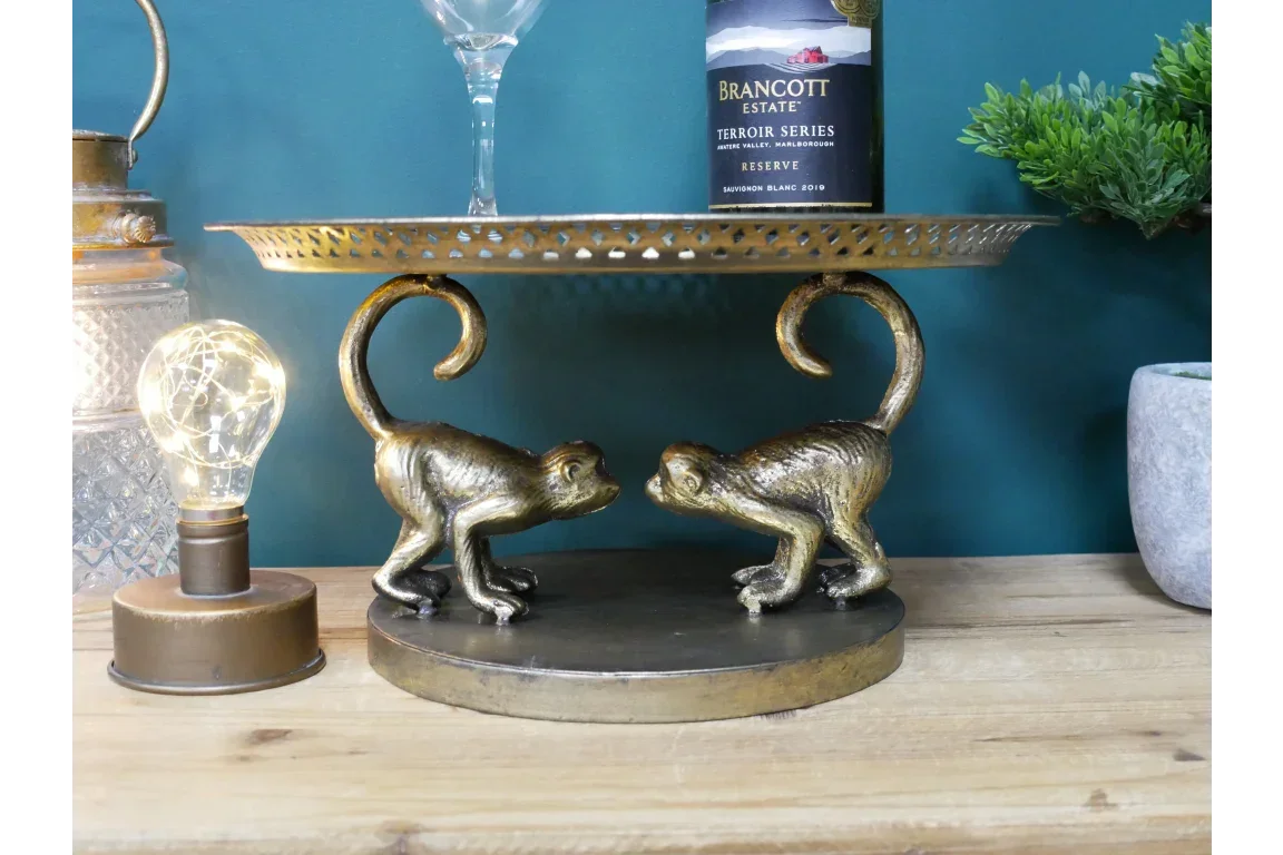 Gold monkey ornament cake stand on wooden table with wine bottle and glass