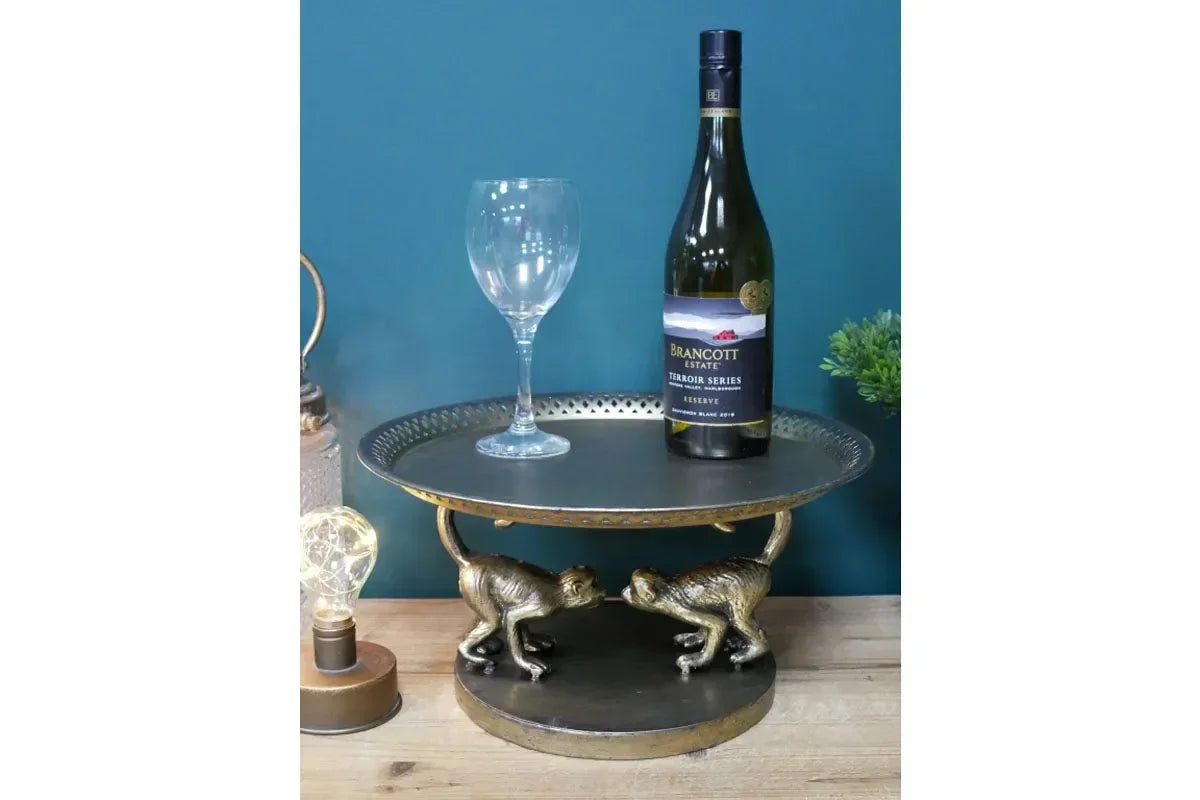Round gold monkey side table with bottle and wine glass, set on wooden surface against teal wall