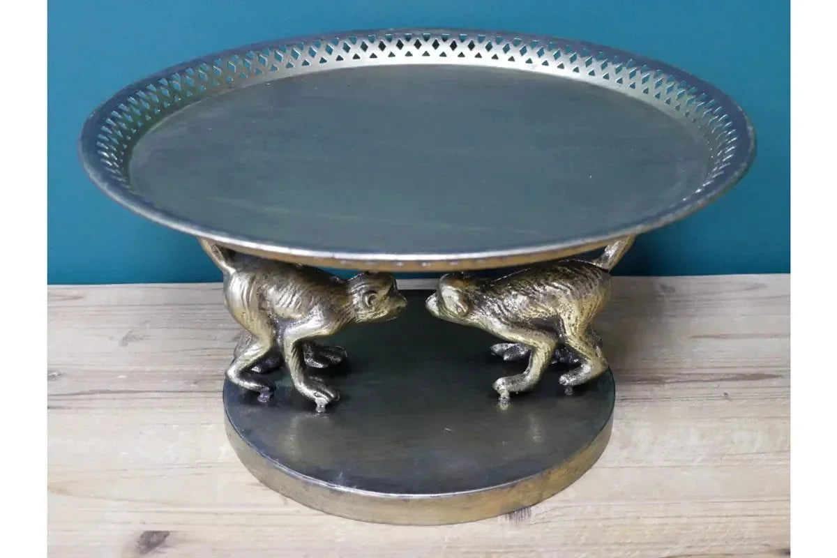Round metal cake stand with brass monkey figurine base on wooden tabletop