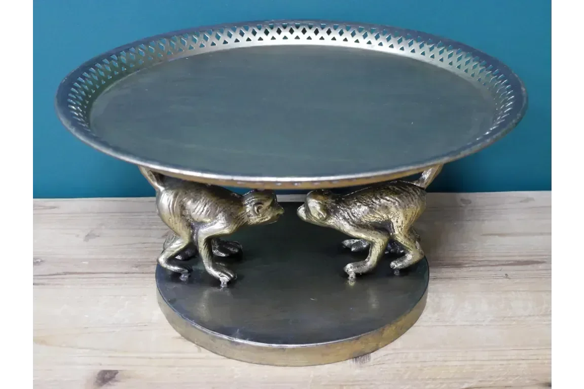 Decorative metal cake stand with gold monkey base on wooden surface