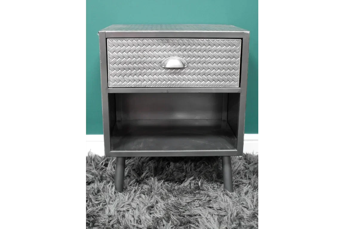 Metal bedside table with textured drawer front and open shelf on shaggy rug