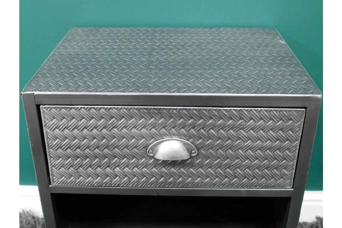 metal bedside table with embossed drawer front and cup handle against a teal wall