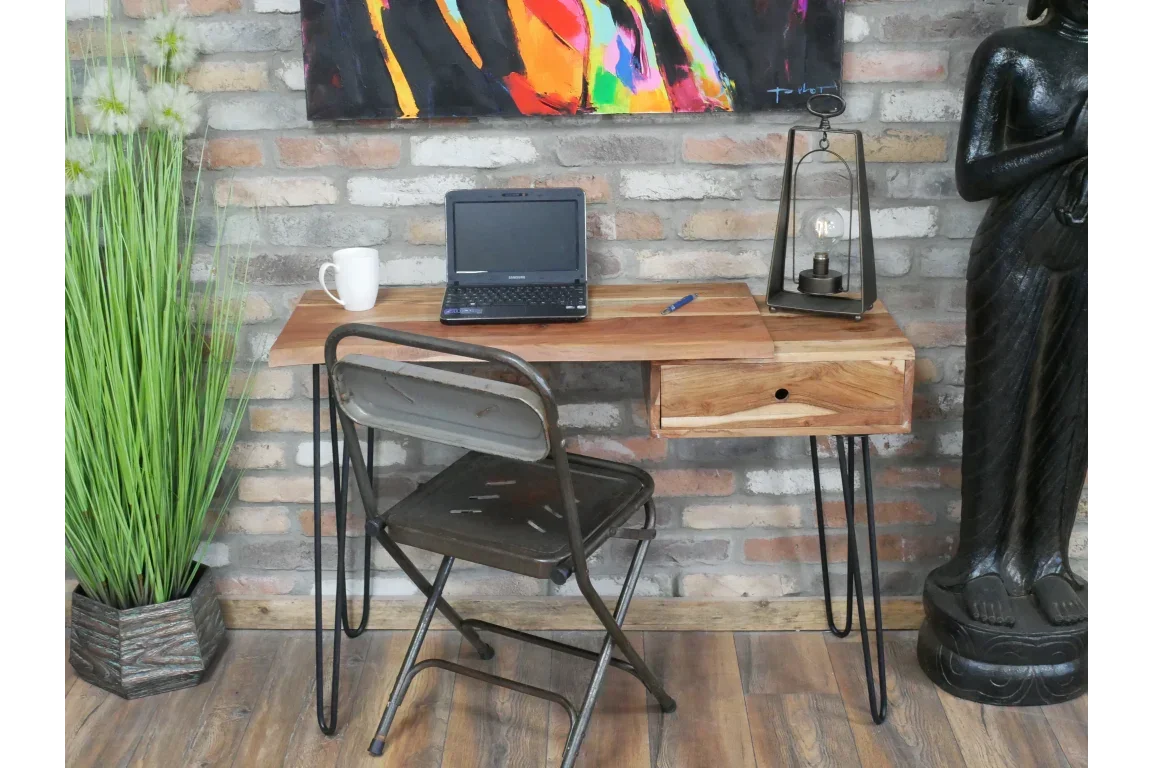 Industrial wooden desk with drawer, laptop, and black metal hairpin legs against brick wall