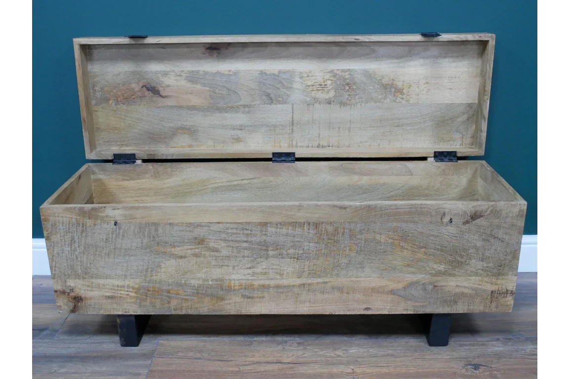 Solid wood storage chest with lift-up lid and black legs on a wooden floor