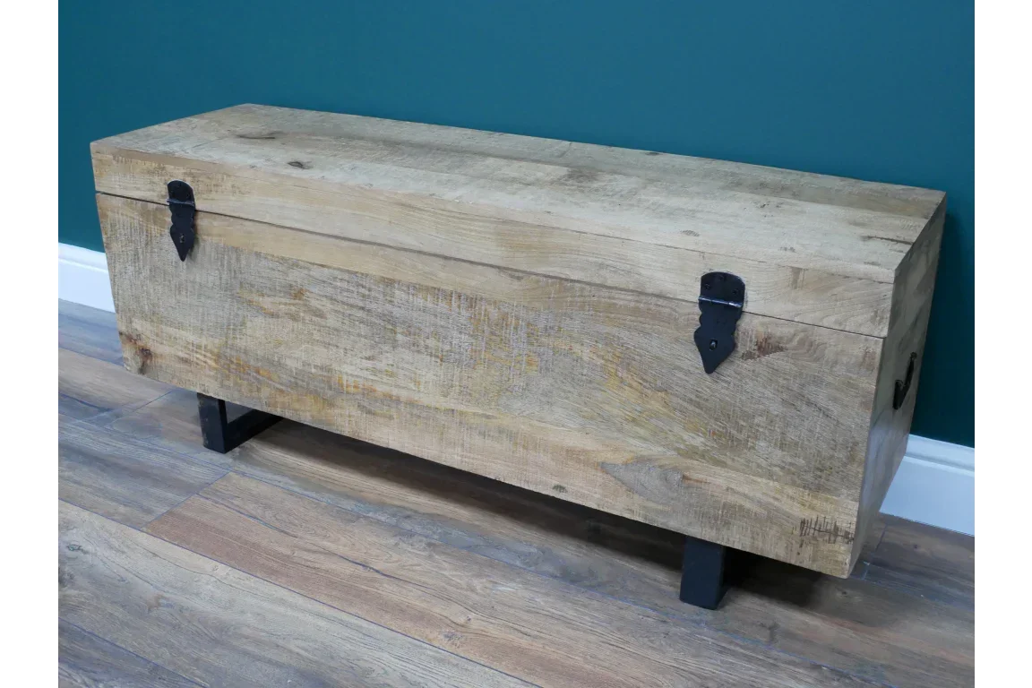 Rustic wooden storage chest with black metal hinges on wood floor against teal wall