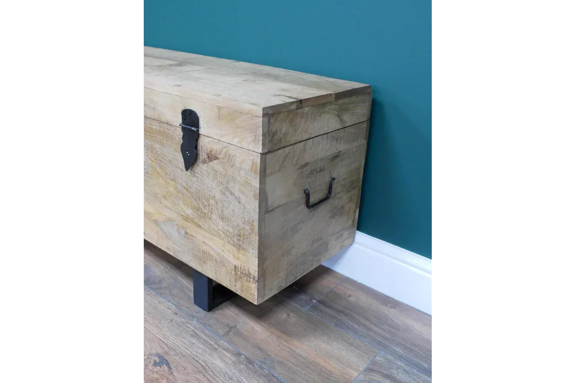 Solid wood storage chest with metal handles and latch, placed on wood flooring against blue wall