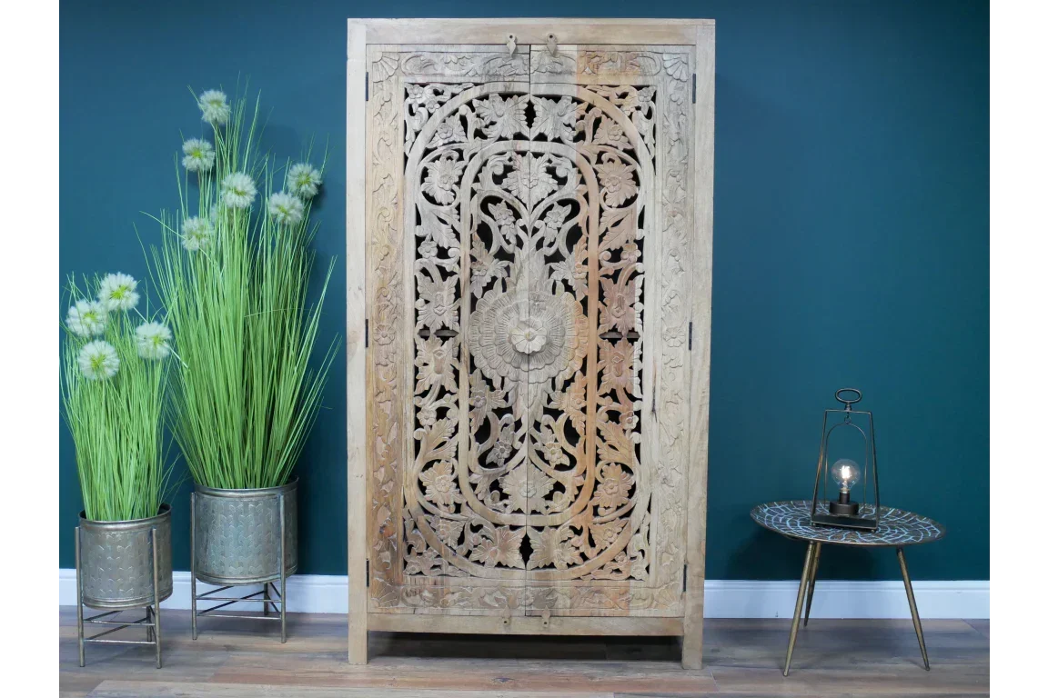 Carved wooden wardrobe with floral pattern, beside metal planters and small round side table