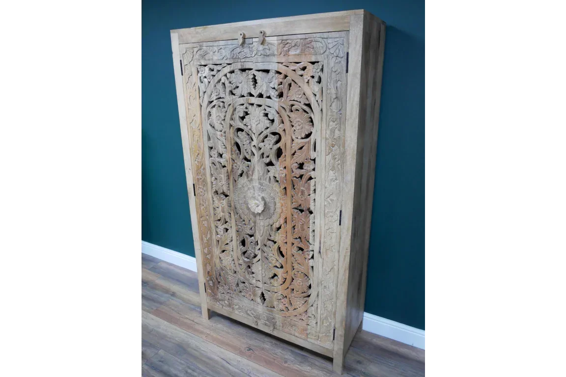Carved solid wood cabinet with intricate floral patterns against teal wall and wood floor