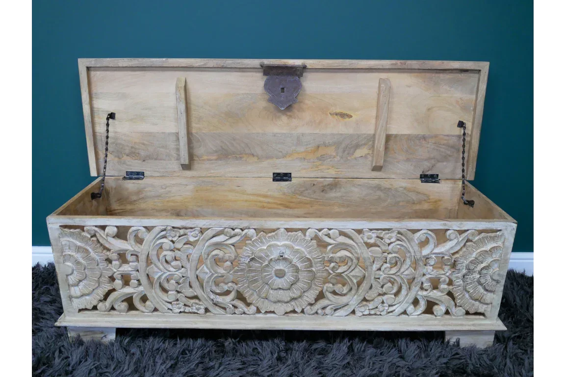 Wooden storage chest with carved floral pattern and open lid on grey rug