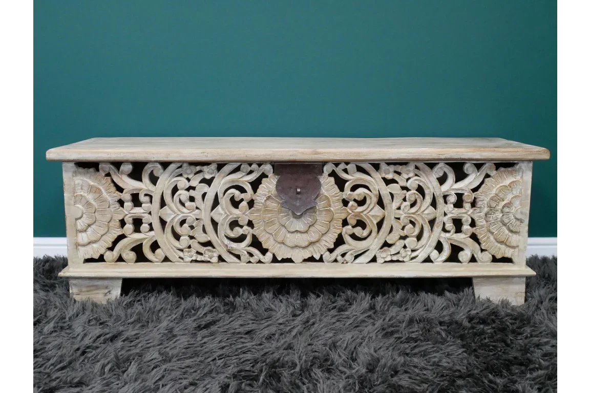 Carved wooden storage chest with floral patterns and metal latch on grey rug