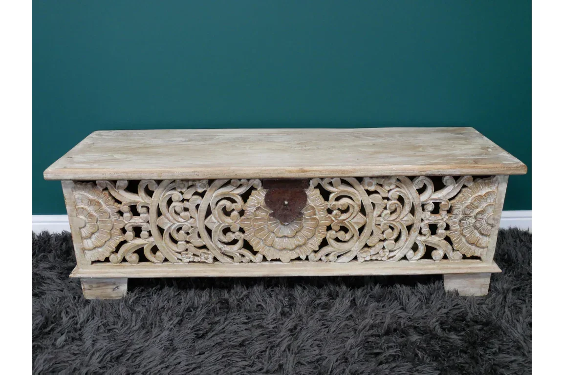 Wooden storage chest with carved floral detailing on front, placed on dark rug
