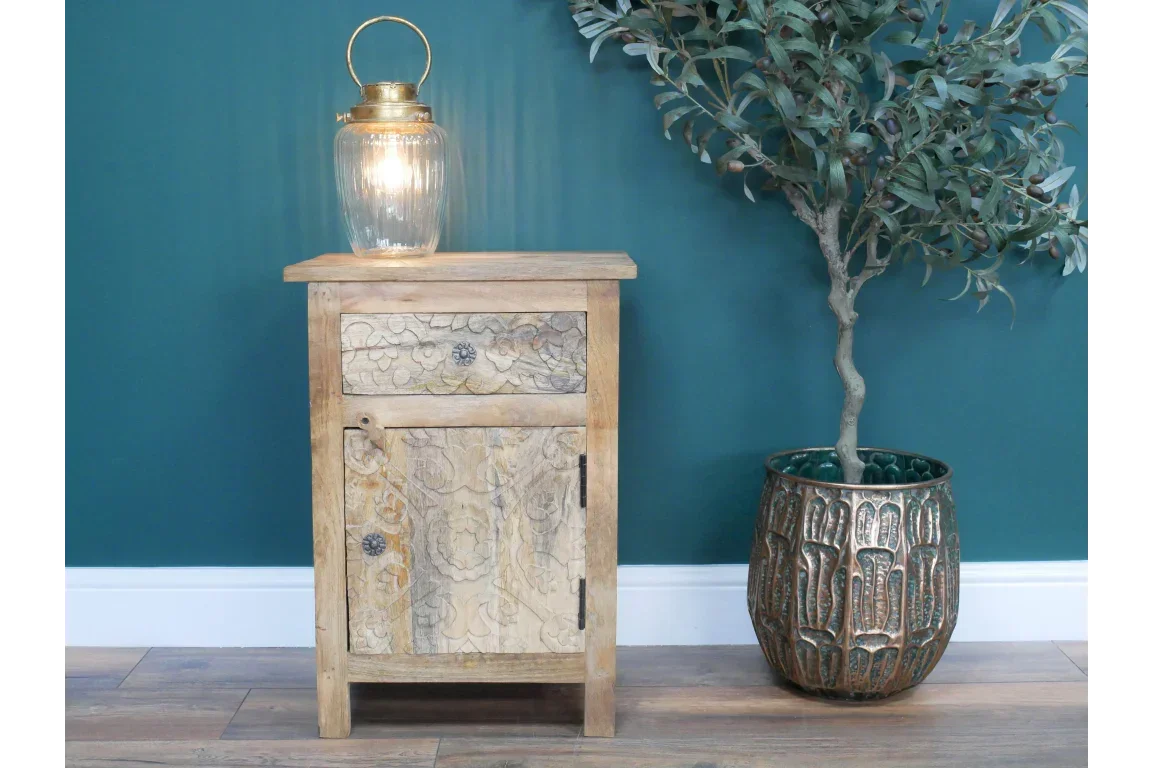 Wooden bedside cabinet with carved floral detail beside green ceramic plant pot