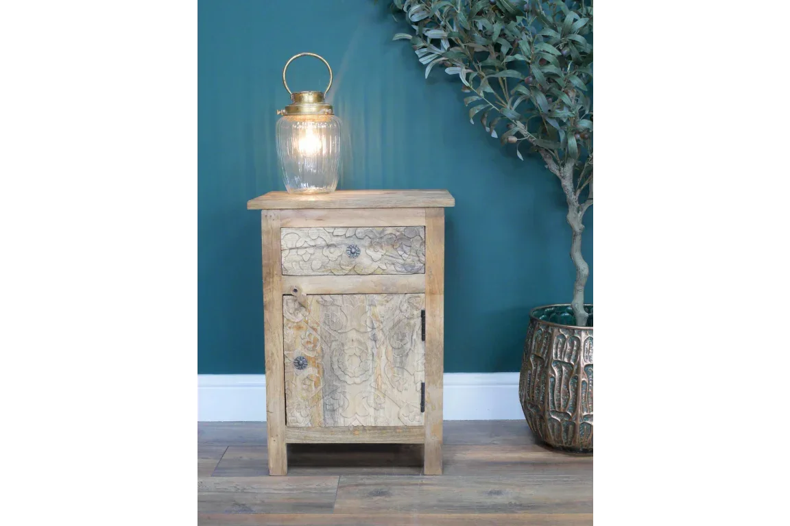 Rustic wooden bedside cabinet with carved drawer, set beside a potted plant and lantern