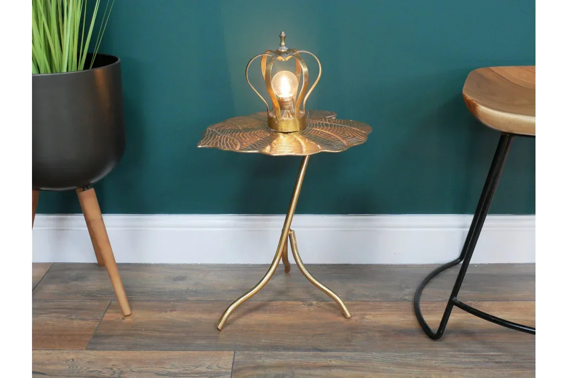Gold leaf side table with decorative lamp, metal base, set against teal wall and wooden floor