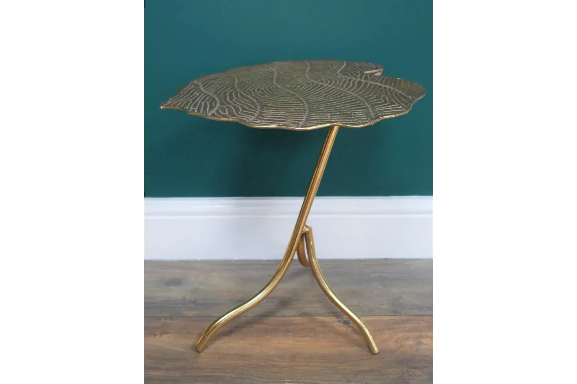 Gold metal side table with leaf-shaped top and curved legs against green wall