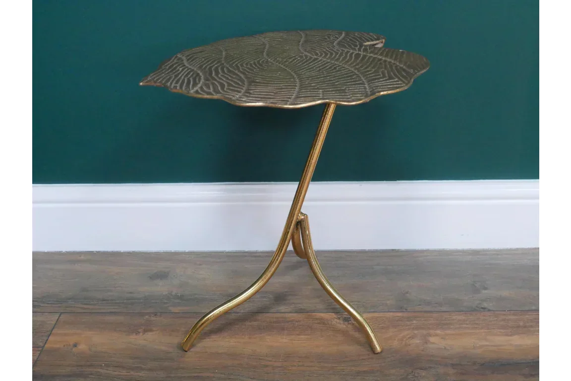 Gold metal accent side table with embossed leaf design and tripod legs on wooden floor