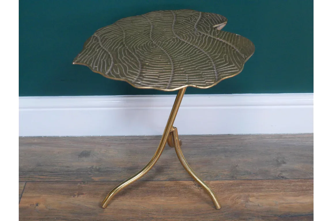 Gold metal side table with leaf-shaped top and three curved legs on wood floor