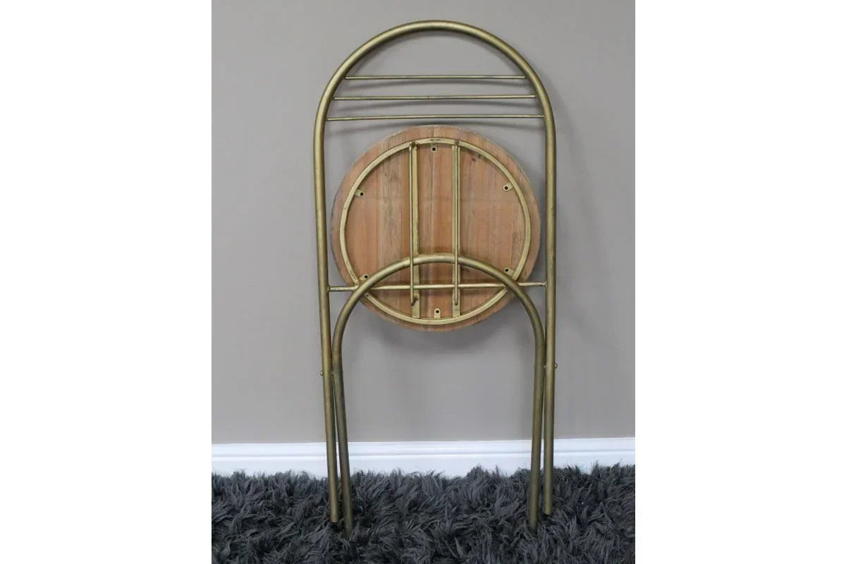 Folding wooden accent table with metal frame, stored upright against a grey wall on carpet