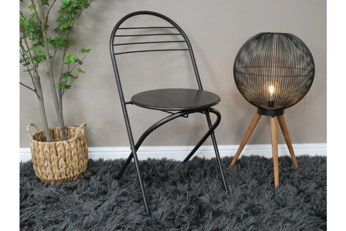 Black metal folding chair on grey rug beside wire floor lamp and woven plant basket