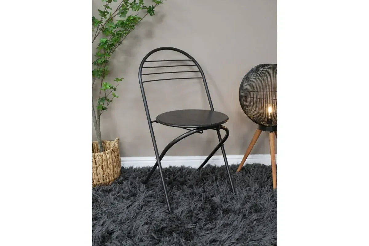 Black metal folding chair on grey shaggy rug with lamp and potted plant nearby