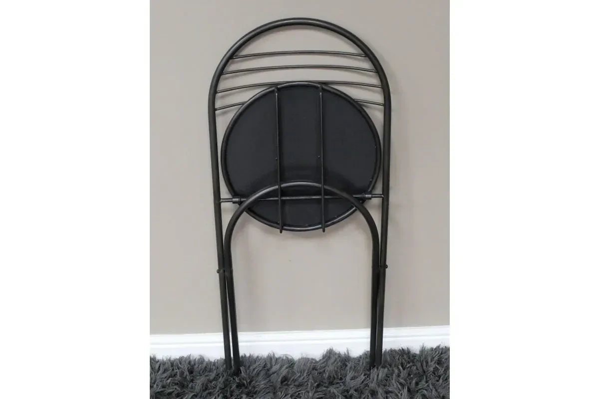 Black metal folding chair with round seat folded against wall on grey carpet