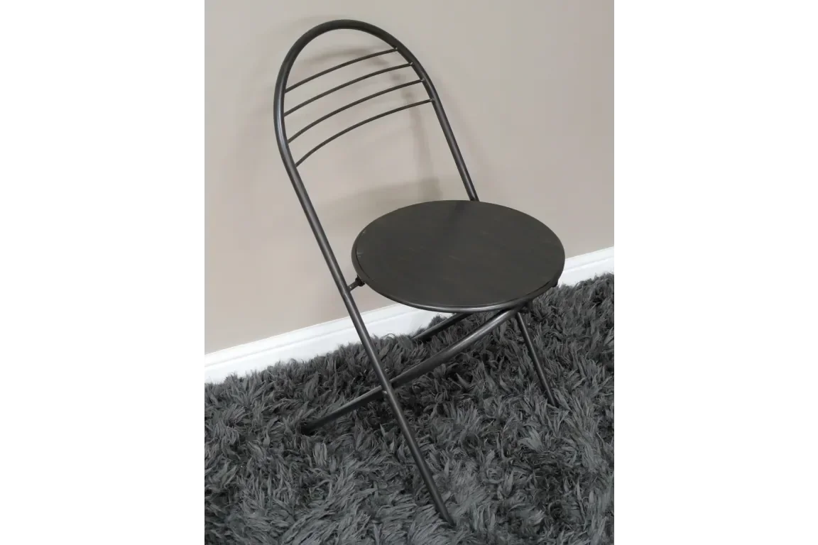 Black metal folding chair with round seat on grey shaggy rug against beige wall